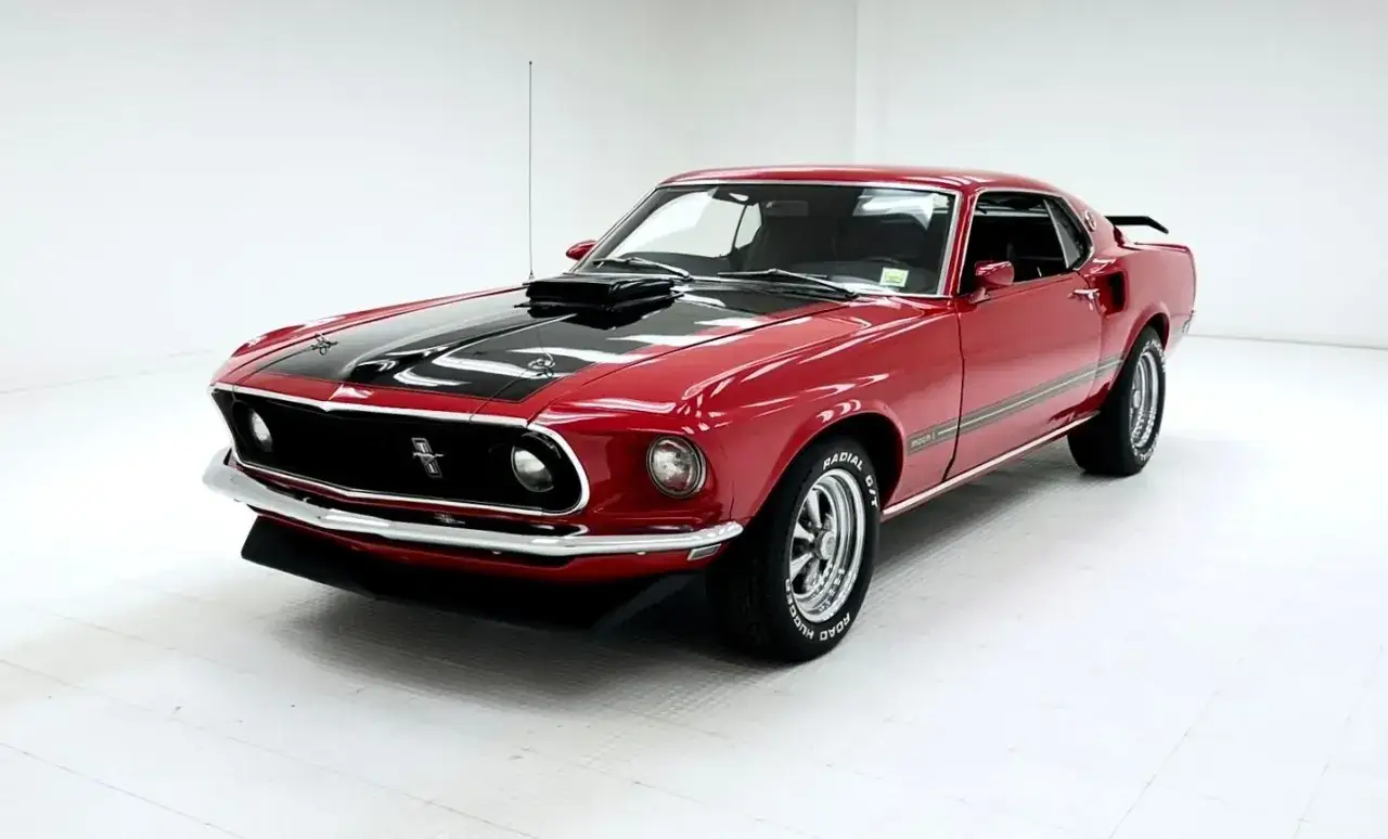 Klasyczny czerwony Ford Mustang 1969 Mach 1 z czarnymi pasami na masce i dachu, gotowy do jazdy.