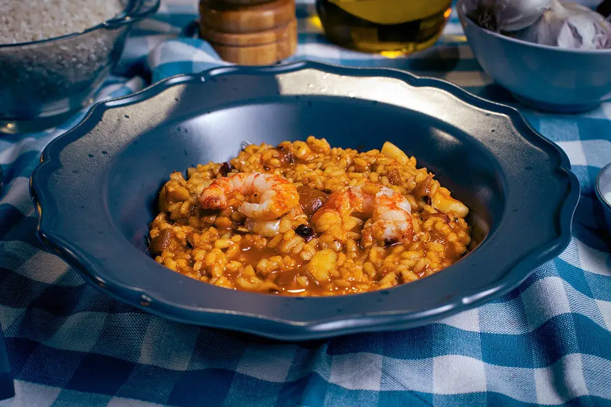 Un delicioso guiso de arroz con gambas y trozos de calamar, servido en un plato azul sobre un mantel a cuadros.