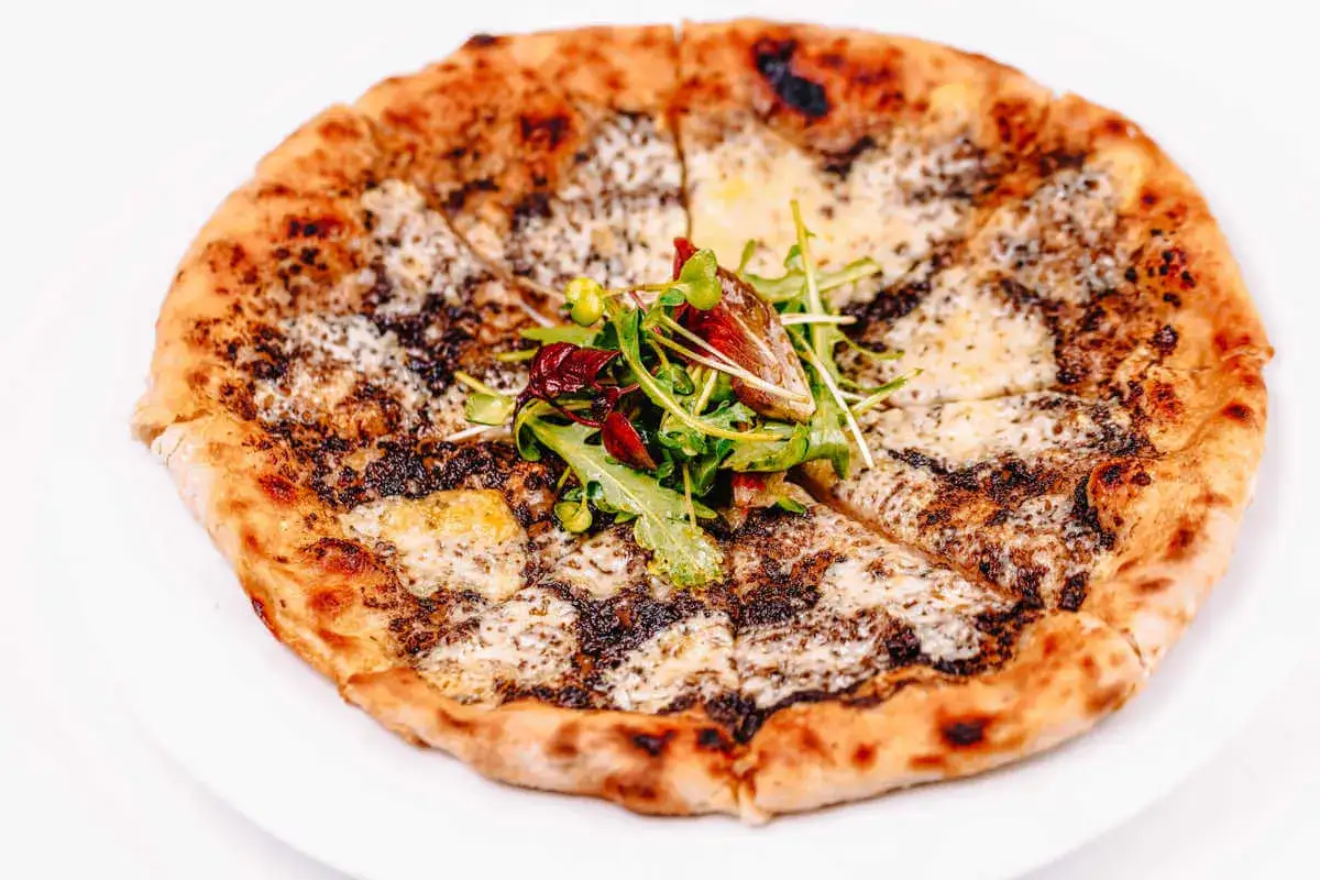 Wykwintna pizza z truflami, serami i świeżą rukolą, podana na białym talerzu.