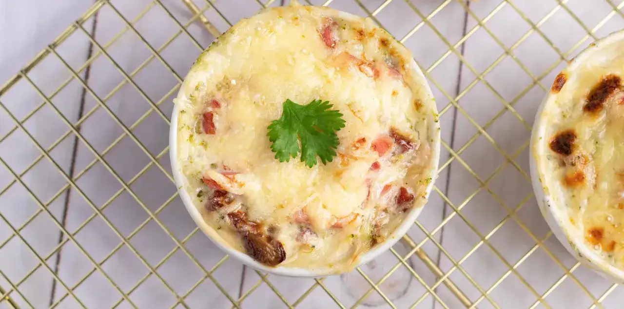 Un gratin de brocolis cr&eacute;meux et dor&eacute;, garni d'une feuille de persil, sur une grille dor&eacute;e.