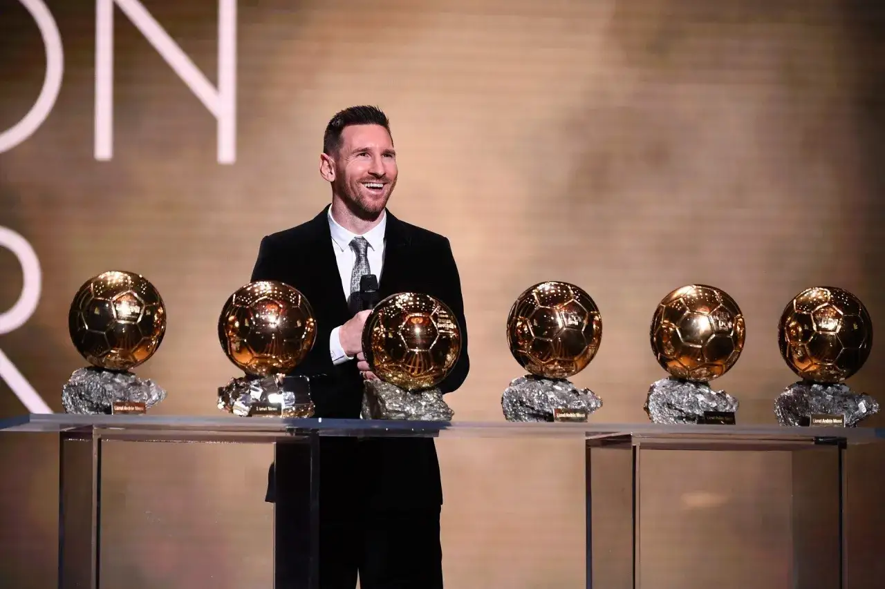 Lionel Messi, uśmiechnięty, trzyma mikrofon obok swoich licznych złotych piłek. Kto ma najwięcej złotych piłek? On!
