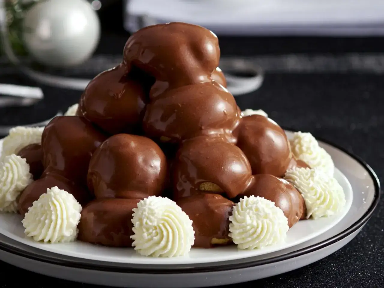 Profitterol ricetta: una piramide di bignè ricoperti di cioccolato fuso, decorata con ciuffi di panna montata.