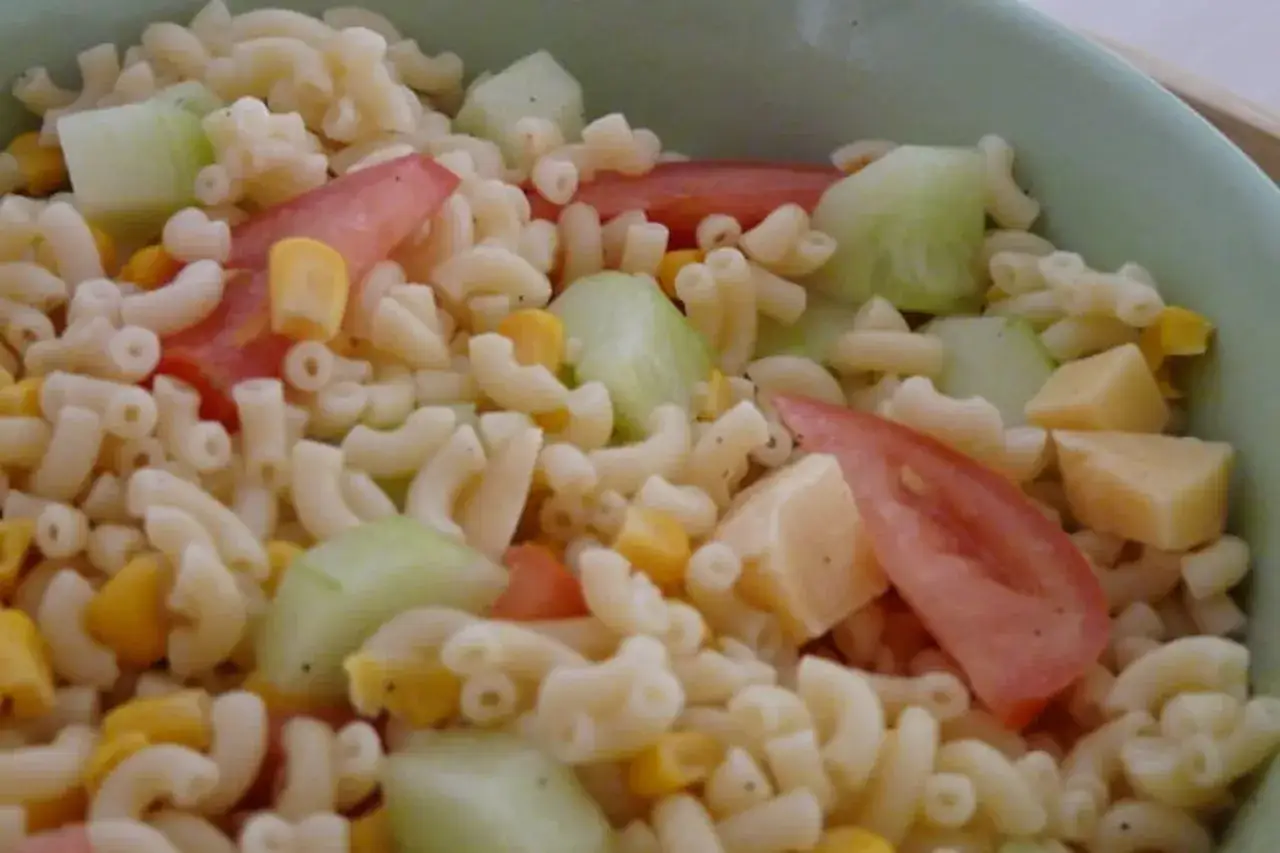 Une salade de pâtes colorée avec des macaronis, des morceaux de concombre, de tomate, de maïs et de fromage.