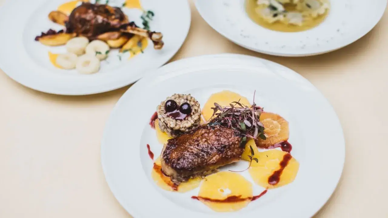 Eleganckie carpaccio z gęsi podane z pomarańczami i kaszą. Obok talerz z pieczoną gęsią i kluskami.