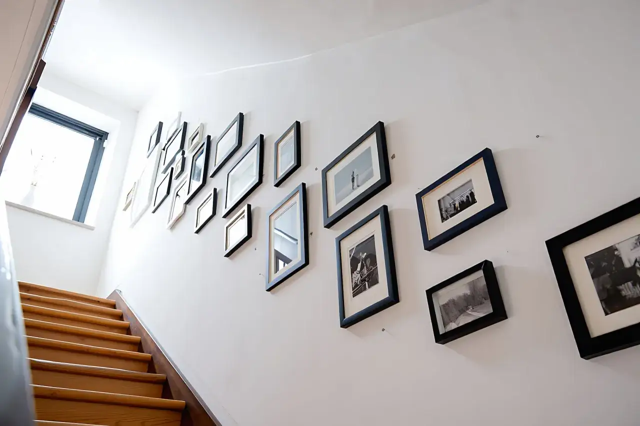 Inspiracja, jak dobrać ramki do domowej galerii zdjęć na klatce schodowej. Różnorodne czarno-białe fotografie w prostych ramach tworzą spójną kompozycję.