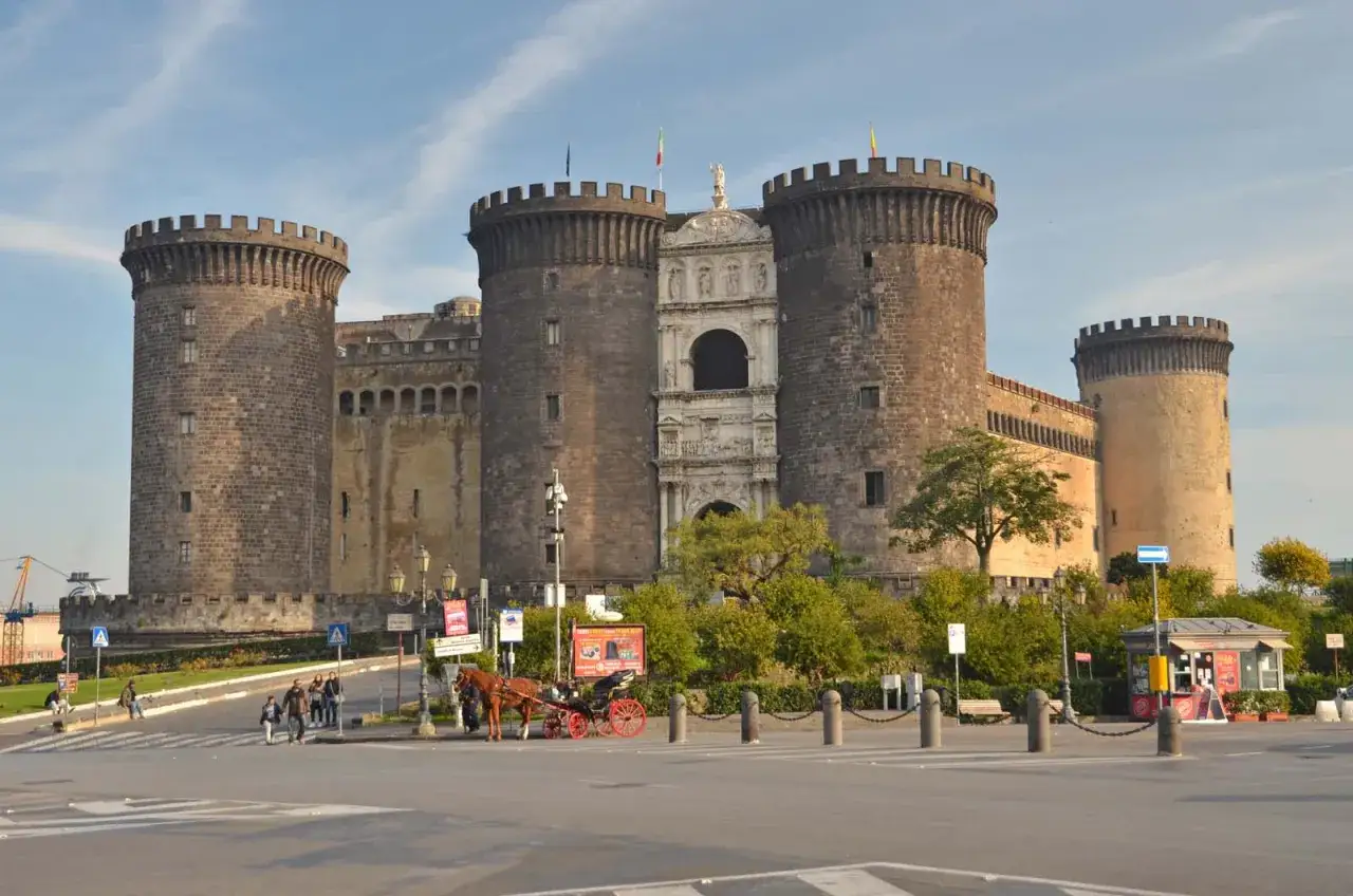 Castel Nuovo w Neapolu, imponująca forteca z wieżami i bramą, to miejsce, które koniecznie trzeba zobaczyć. Obok przechadza się turysta z dorożką.