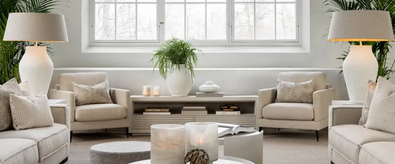 En ljus och luftig lounge med bekv&auml;ma f&aring;t&ouml;ljer i Newport-stil, prydda med dekorativa kuddar. En stor gr&ouml;n v&auml;xt och stilrena lampor skapar en harmonisk atmosf&auml;r.