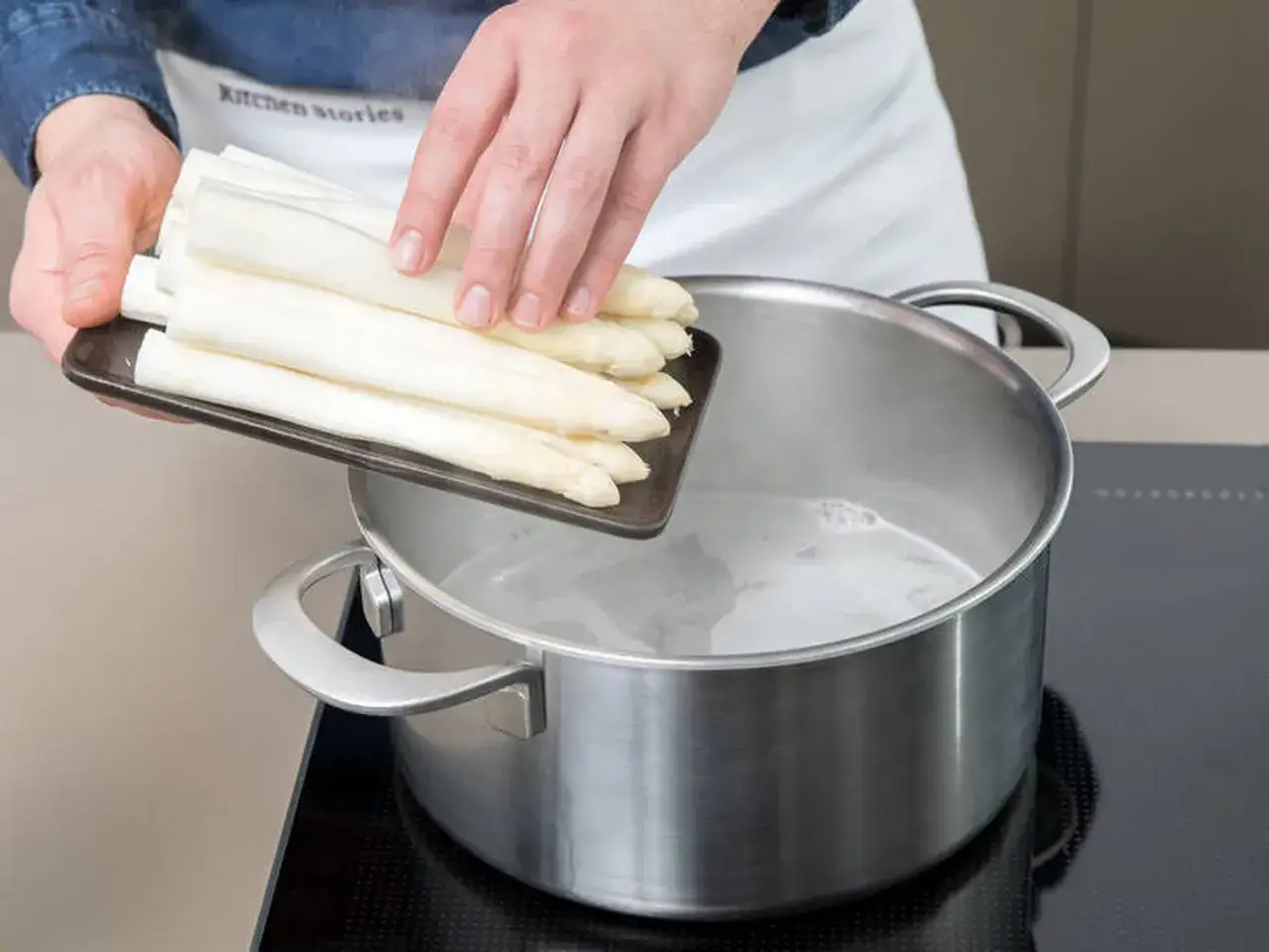 Hände legen weißen Spargel in kochendes Wasser. Perfekt zum Spargel kochen!