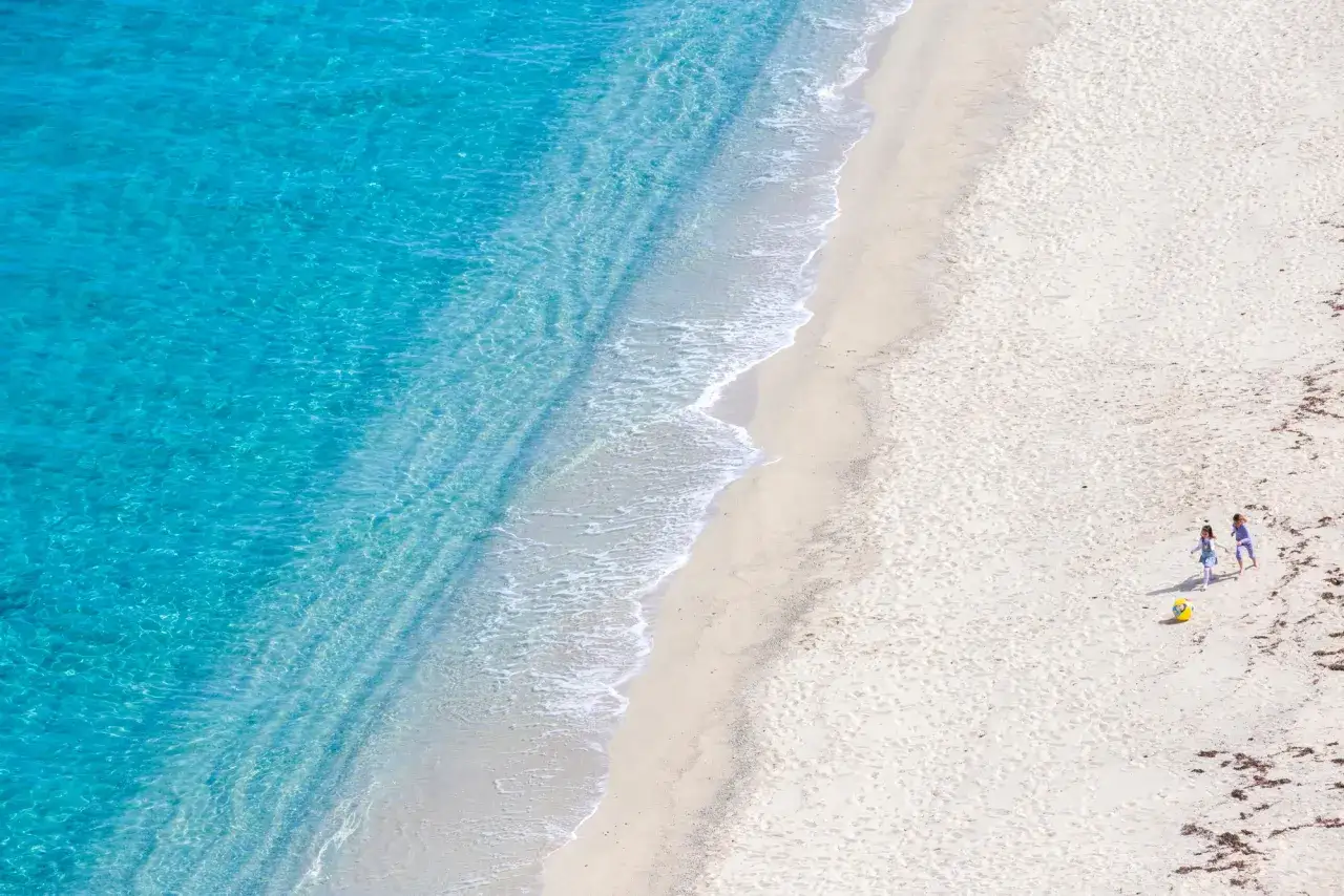 Due bambini giocano sulla sabbia dorata vicino al mare cristallino del Capo Vaticano, Tropea.