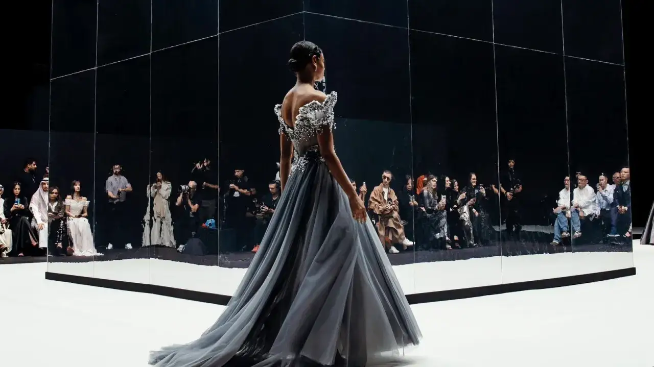 A model walks the runway in a flowing grey gown, showcasing Saudi Arabian fashion.