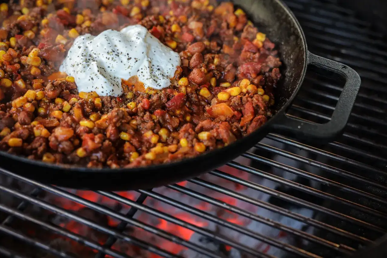 Gorące chili con carne przepis w żeliwnej patelni na grillu, z kleksem śmietany na wierzchu.