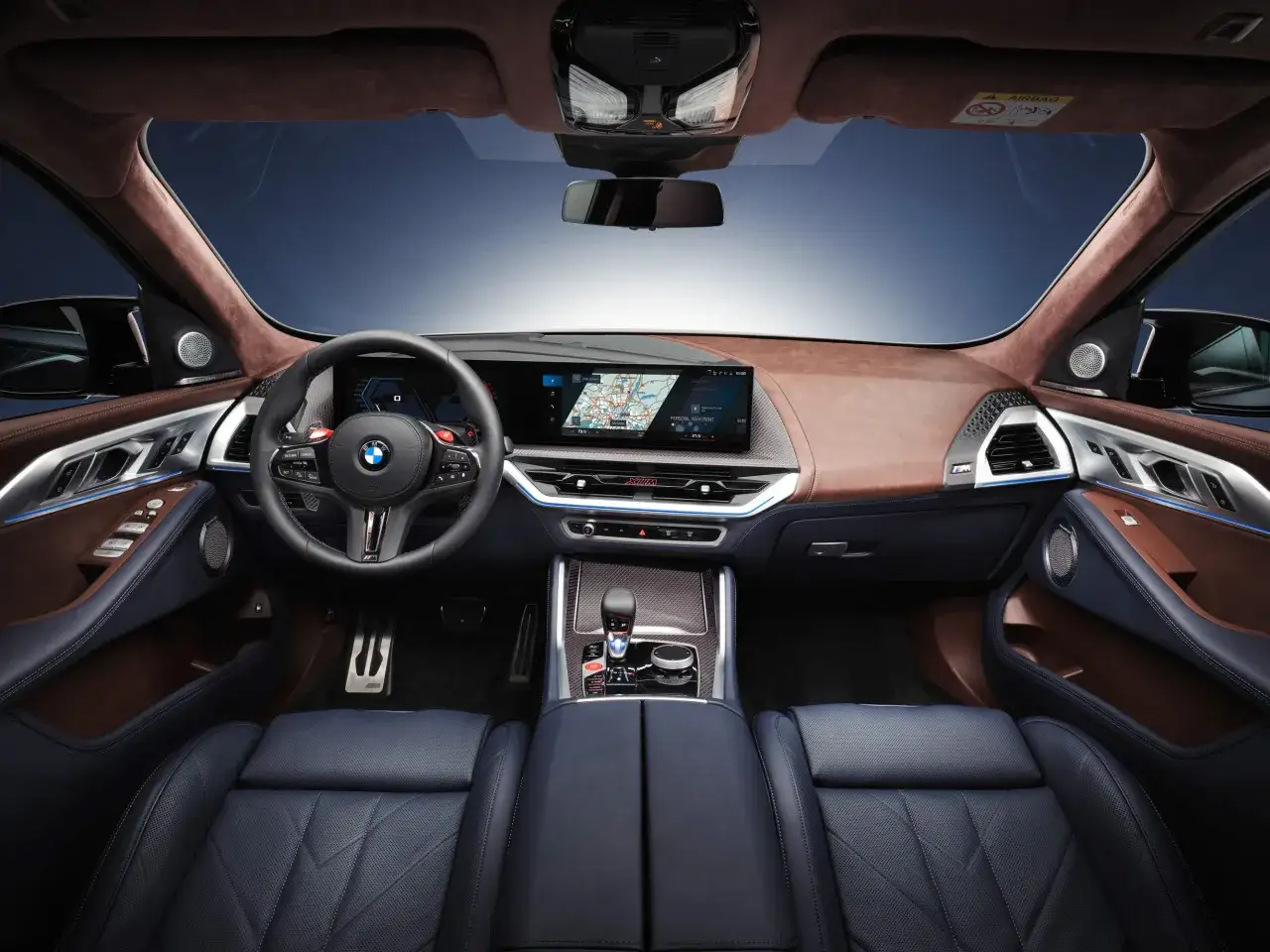 Wnętrze BMW XM: skórzana tapicerka, nowoczesny kokpit z ekranem nawigacji i cyfrowymi zegarami, sportowa kierownica.
