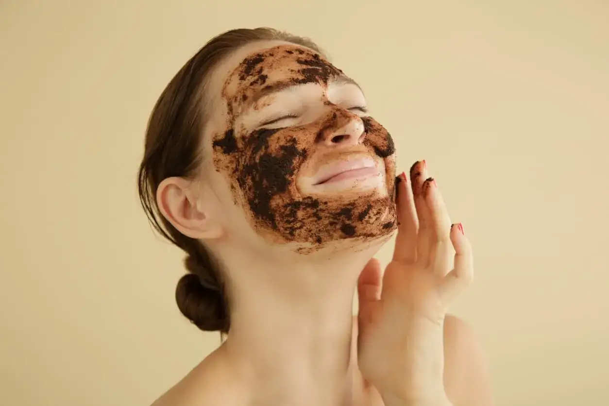 Mujer con mascarilla de caf&eacute; en la cara, aprendiendo como exfoliar la cara para una piel radiante.