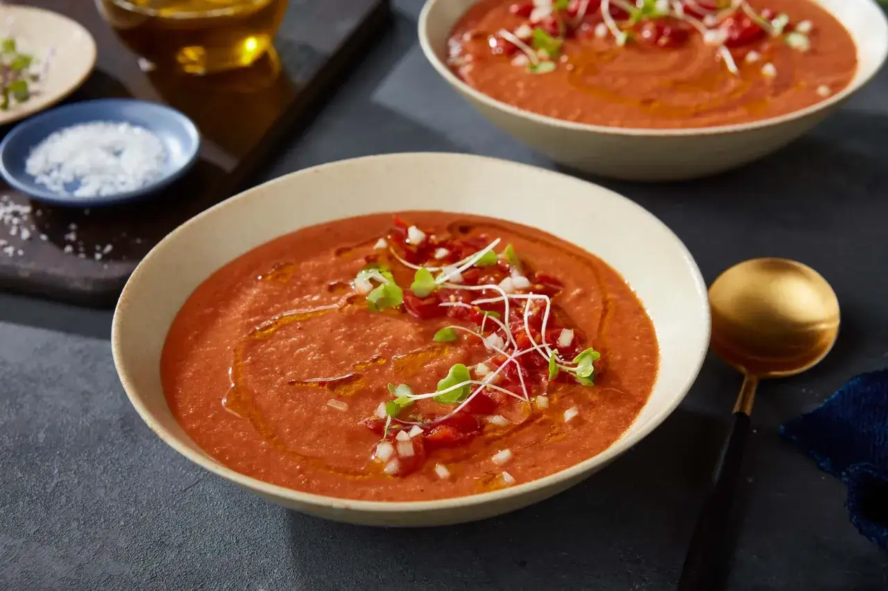 En skål med krämig tomatsoppa, perfekt för ett enkelt tomatsoppa recept. Garnerad med tärnad tomat, lök och groddar.