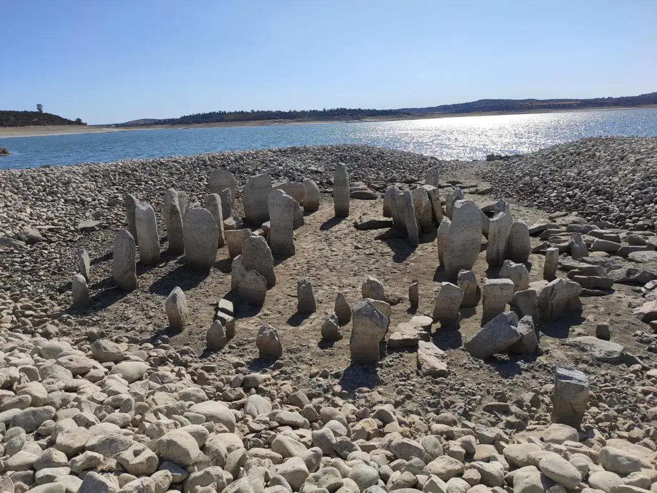 El dolmen de Guadalperal emerge de las aguas bajas, un círculo de piedras ancestrales bajo un cielo azul.