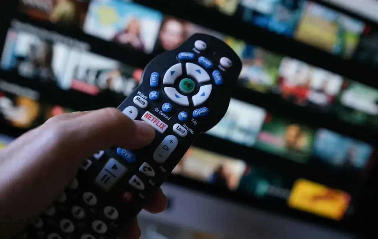 Dłoń trzyma pilot z przyciskiem Netflix, gotowa do nauki, jak zainstalować Netflixa na telewizorze, by cieszyć się filmami.
