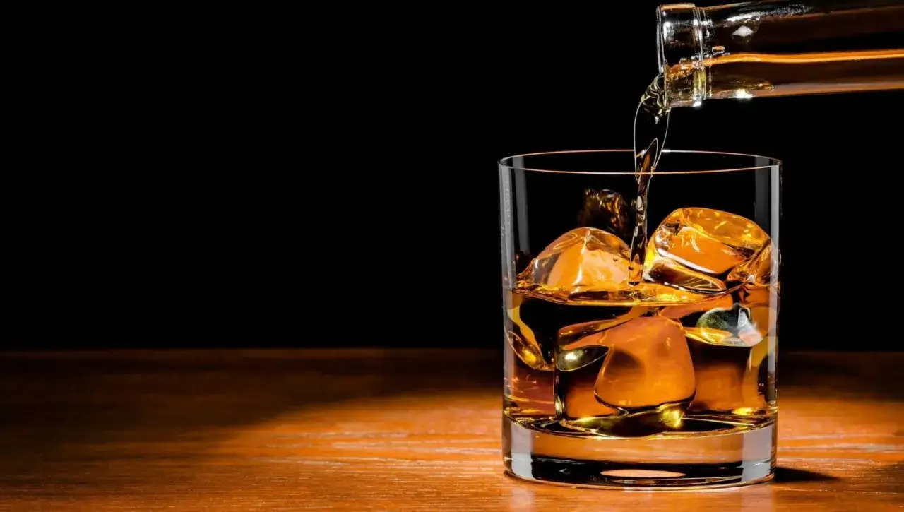 Whisky z colą, ile kalorii ma ten drink? Bursztynowy płyn z lodem w szkle, nalewany z butelki.