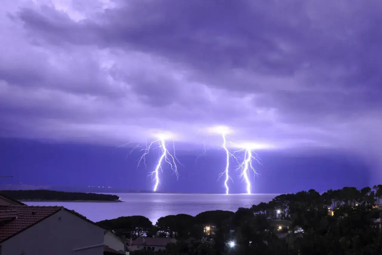 Gewaltiger **blitz donner entfernung** erhellt den violetten Himmel über dem Meer. Ein Sturm zieht auf, während Blitze die Nacht durchzucken.