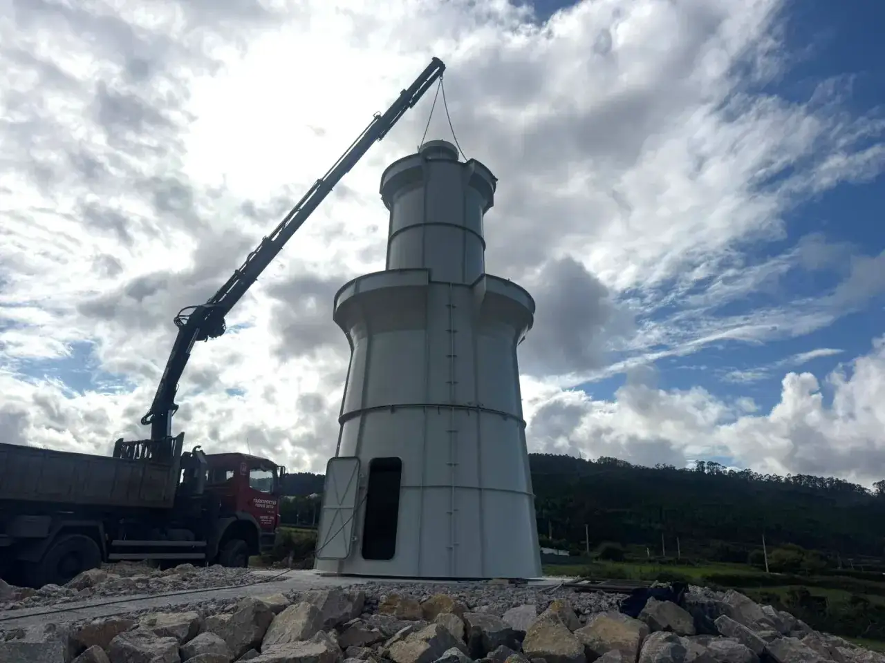 Gr&uacute;a elevando una estructura cil&iacute;ndrica, parte del rompeolas de Burela, sobre un cami&oacute;n.