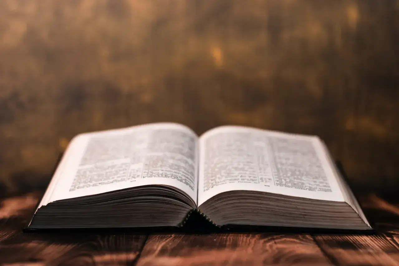 An open Bible on a wooden table, its pages filled with text, invites contemplation on whether cursing is a sin.