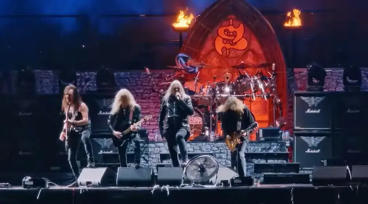 Le groupe Saxon en pleine performance, avec des guitares, une batterie et un chanteur charismatique sur scène.