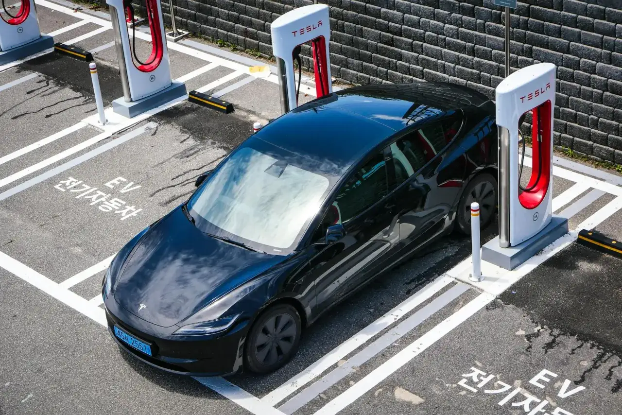Czarny Tesla na stacji ładowania. Zastanawiasz się, jak długo ładuje się Tesla? Czas ładowania zależy od modelu i ładowarki.