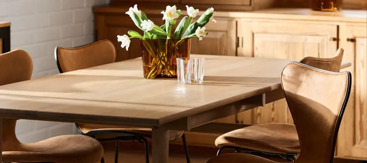 Ett ljust tr&auml;bord med klassiska designstolar i l&auml;der. En vas med vita blommor och glas st&aring;r p&aring; bordet.