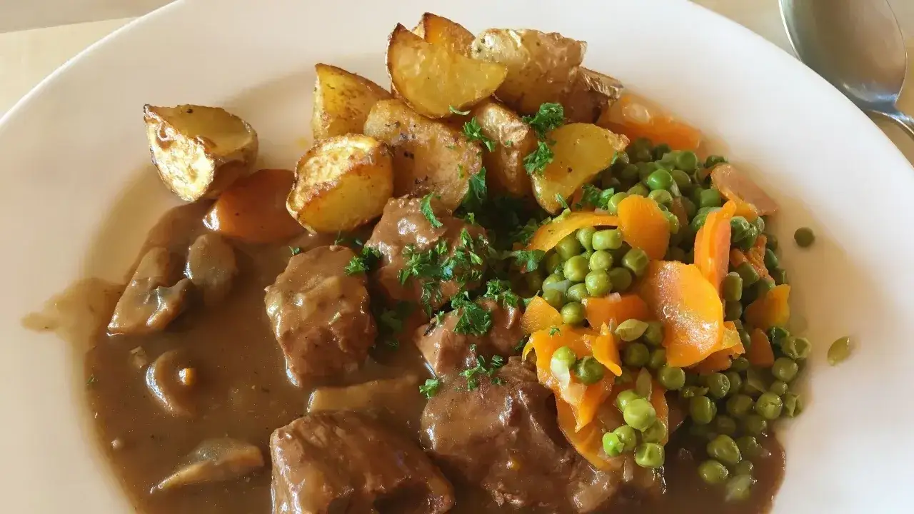 Un saporito spezzatino con piselli, carote e patate arrosto, guarnito con prezzemolo fresco. Un piatto confortante e delizioso.