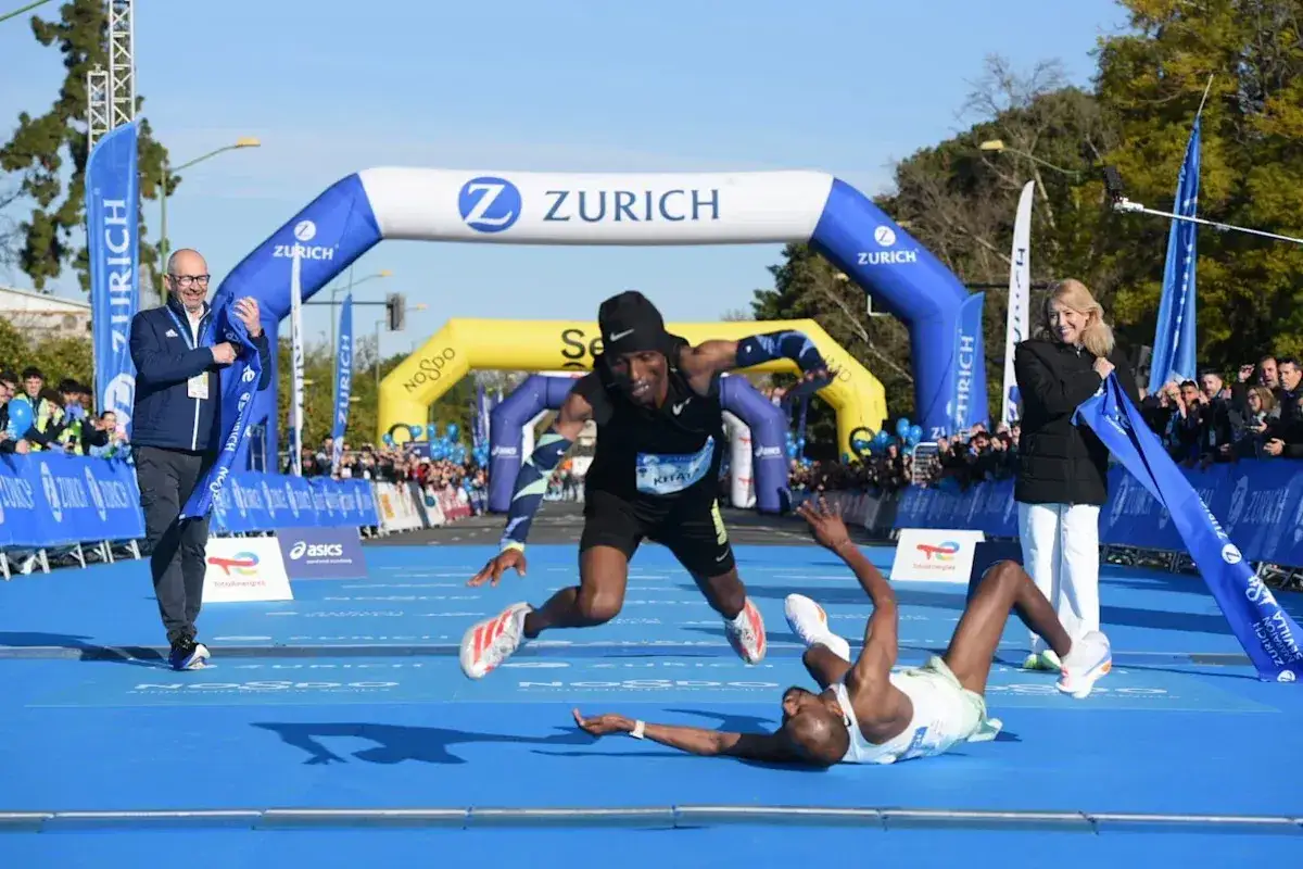 Llegada dram&aacute;tica en el marat&oacute;n Sevilla 2026. Un corredor cae mientras otro cruza la meta bajo el arco de Zurich.