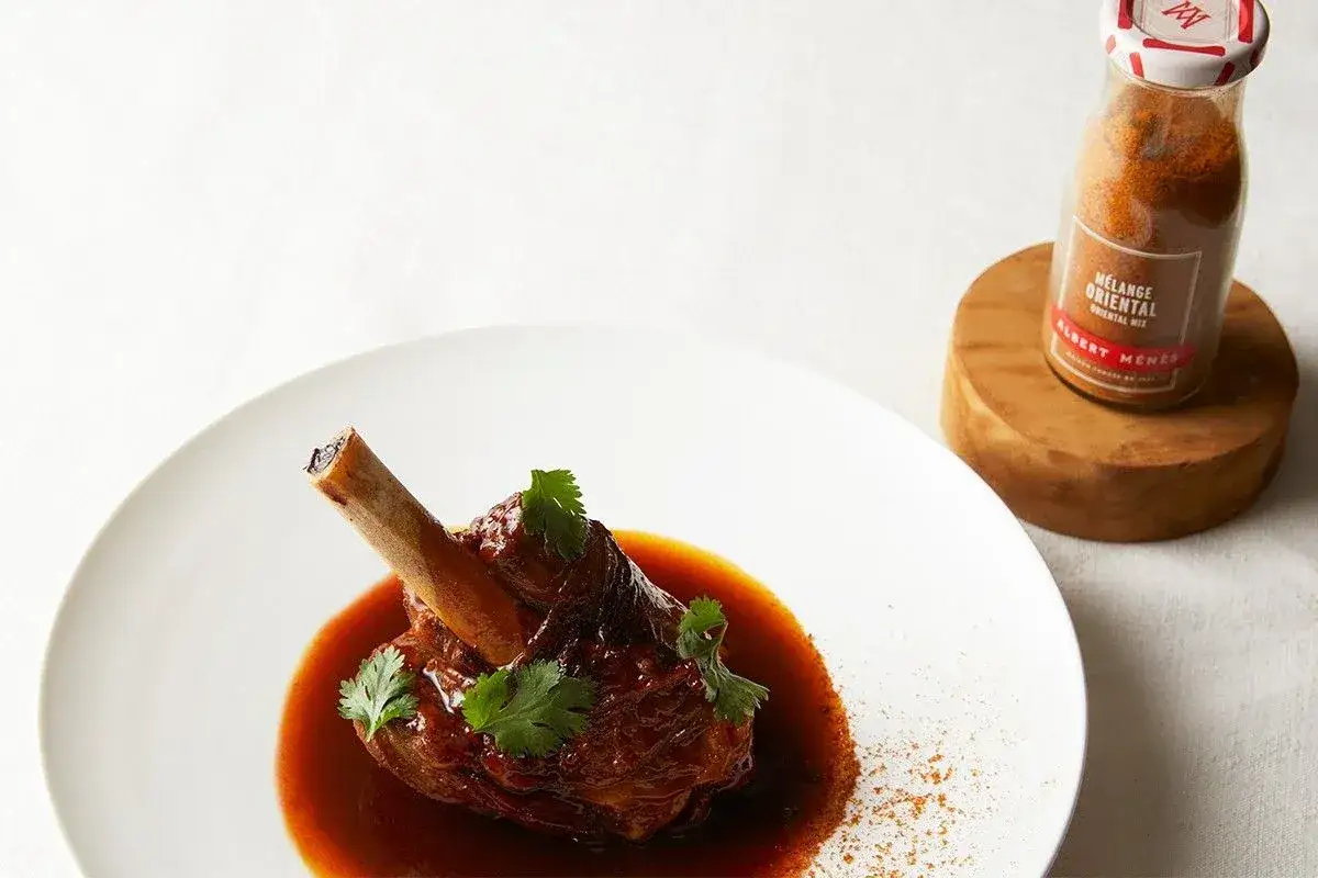 Souris d'agneau confite, napp&eacute;e d'une sauce riche et garnie de coriandre fra&icirc;che. Un m&eacute;lange oriental Albert M&eacute;n&egrave;s &agrave; proximit&eacute; sugg&egrave;re une touche d'&eacute;pices.