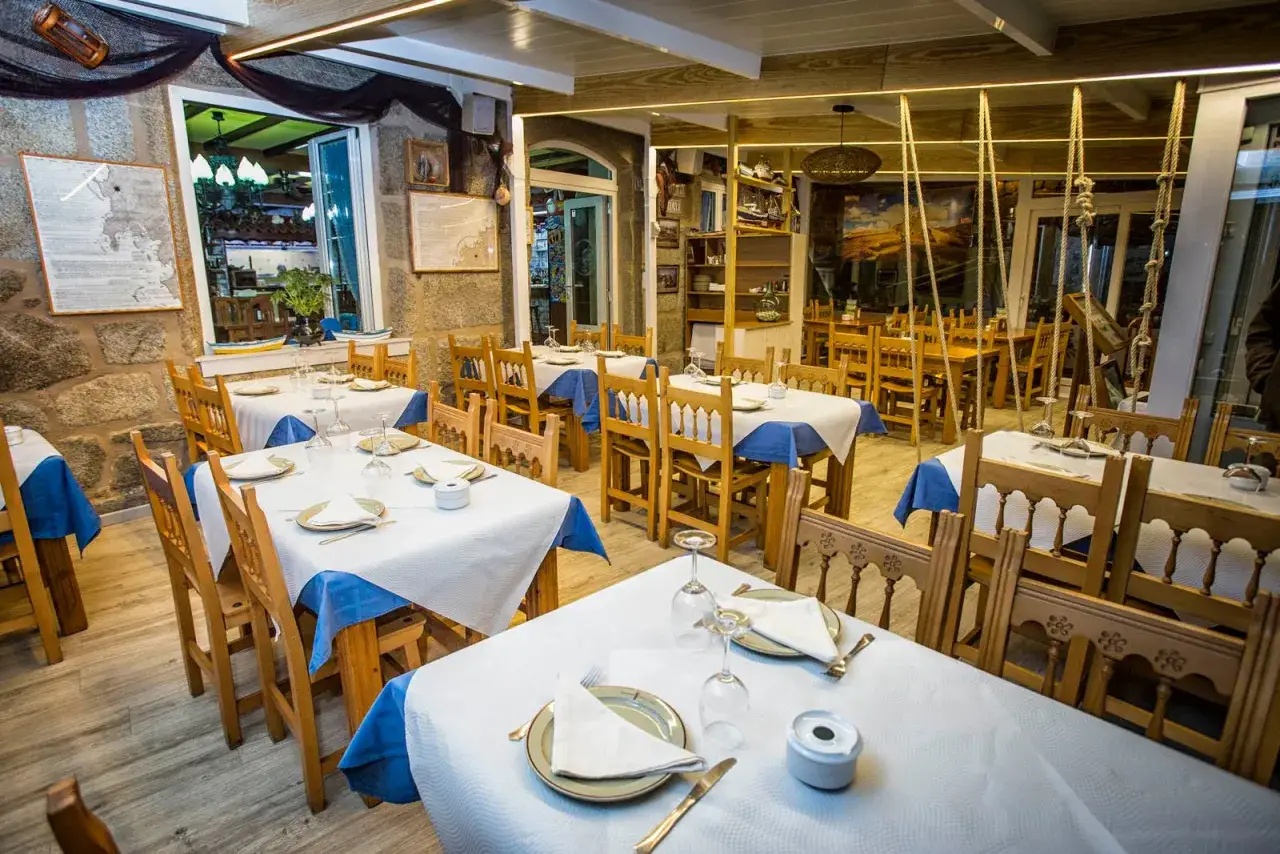 Mesas puestas en un restaurante marinero, ideal para comer en Muxía. Decoración rústica con redes y mapas.