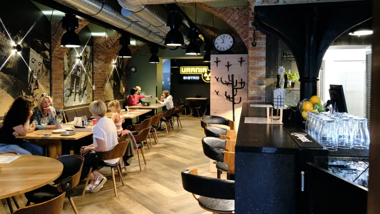 Wnętrze restauracji Urania Bistro z ludźmi przy stołach i barem.