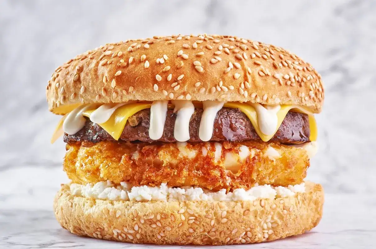 Apetyczny burger drwala przepis: soczysta wołowina, chrupiące panierowane ziemniaki, ser i biały sos na sezamowej bułce.