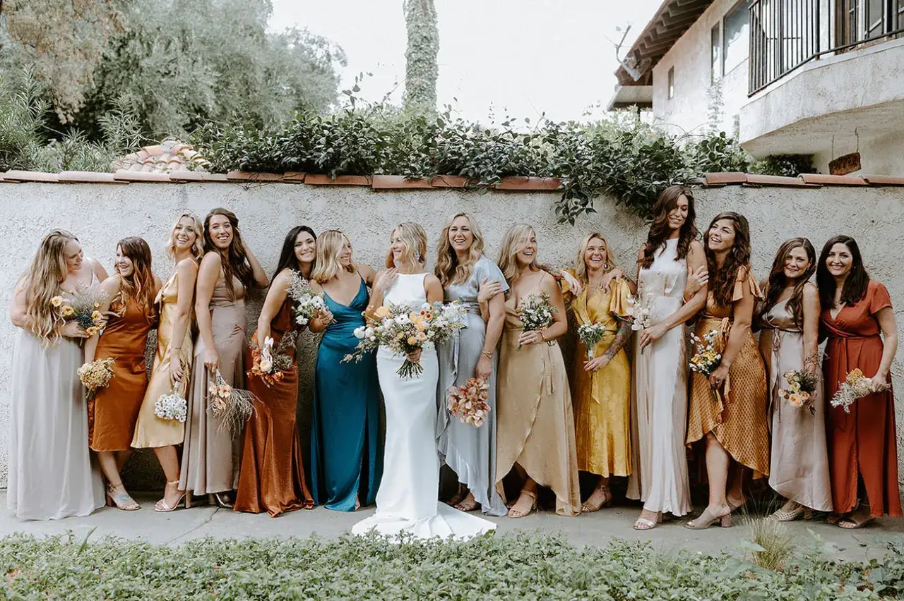 Un groupe de demoiselles d'honneur souriantes, v&ecirc;tues de robes aux couleurs vives, pose devant un mur en pierre.