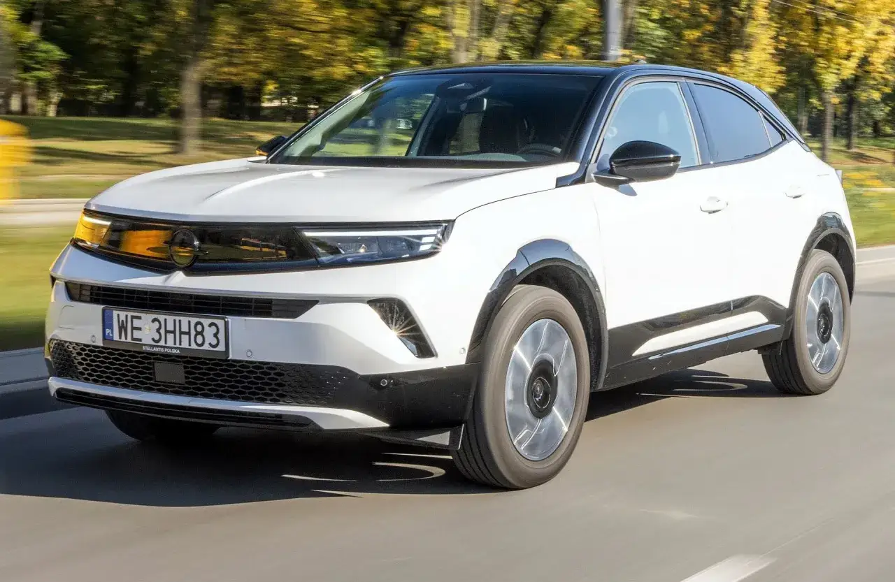 Biały Opel Mokka z czarnym dachem jedzie po drodze. Sprawdź aktualną opel mokka cena i wybierz swój wymarzony samochód.
