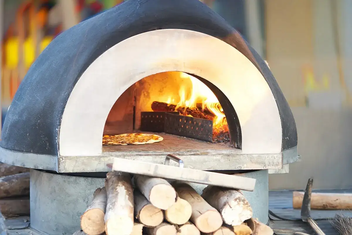 En pizza bakas i en vedeldad ugn. Elden sprakar och ger v&auml;rme till den perfekta pizza p&aring; muurikka.