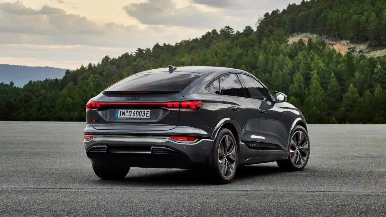 Elegancki Audi Q6 e-tron w ciemnym kolorze, z charakterystycznym pasem świateł z tyłu, na tle leśnego krajobrazu. Sprawdź audi q6 e-tron cena.
