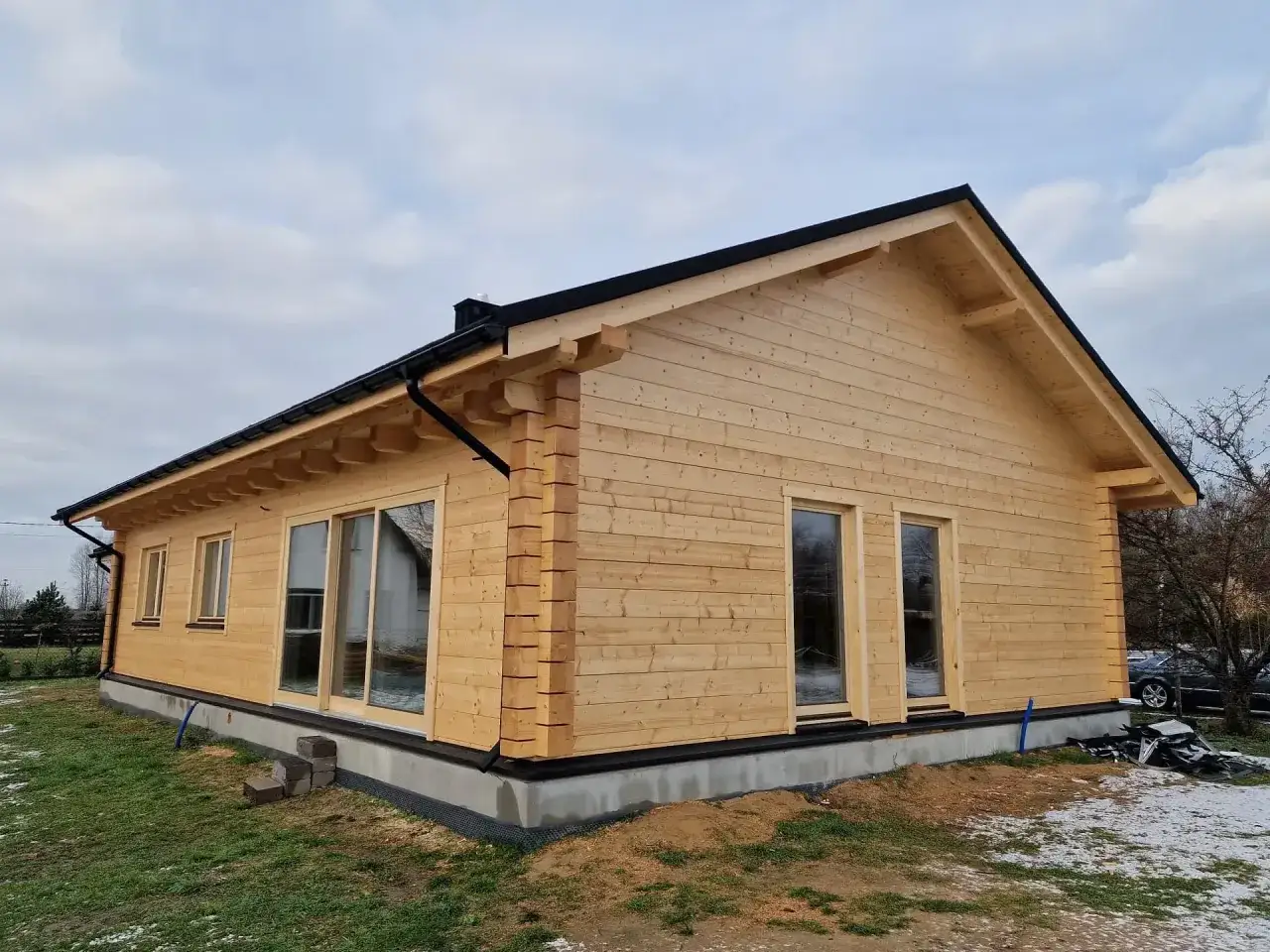 Nowy dom z bali drewnianych, z dużymi oknami i czarnym dachem. Grubość bala na dom całoroczny jest kluczowa dla izolacji.