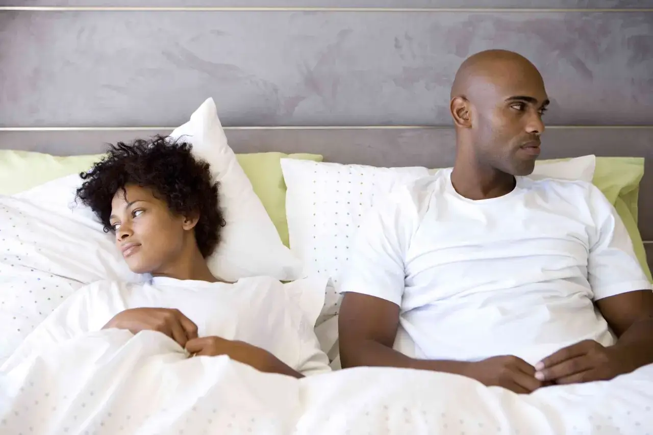 Un couple dans un lit, visiblement distant. L'homme, chauve, regarde ailleurs, suggérant une baisse de libido homme.