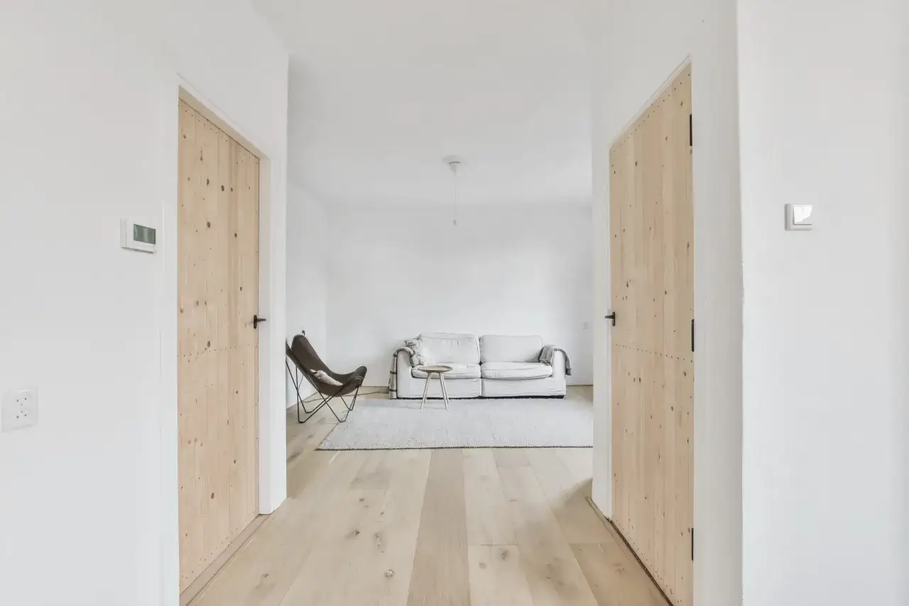 Ingresso di una casa in stile scandinavo con porte in legno chiaro, un divano bianco e una poltrona marrone.