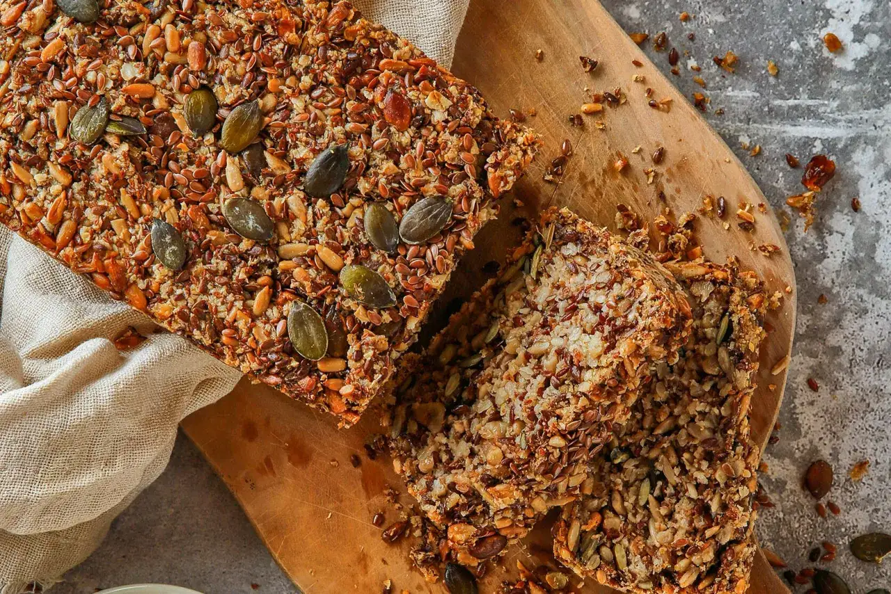 Brot ohne Mehl, reich an Saaten wie Kürbis- und Leinsamen, auf einem Holzbrett.