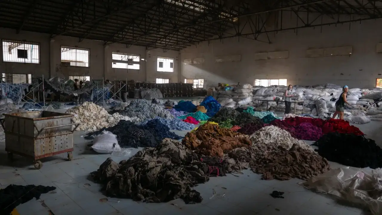 Montones de textiles de colores en un almac&eacute;n, reflejo de las **fast fashion consecuencias**.