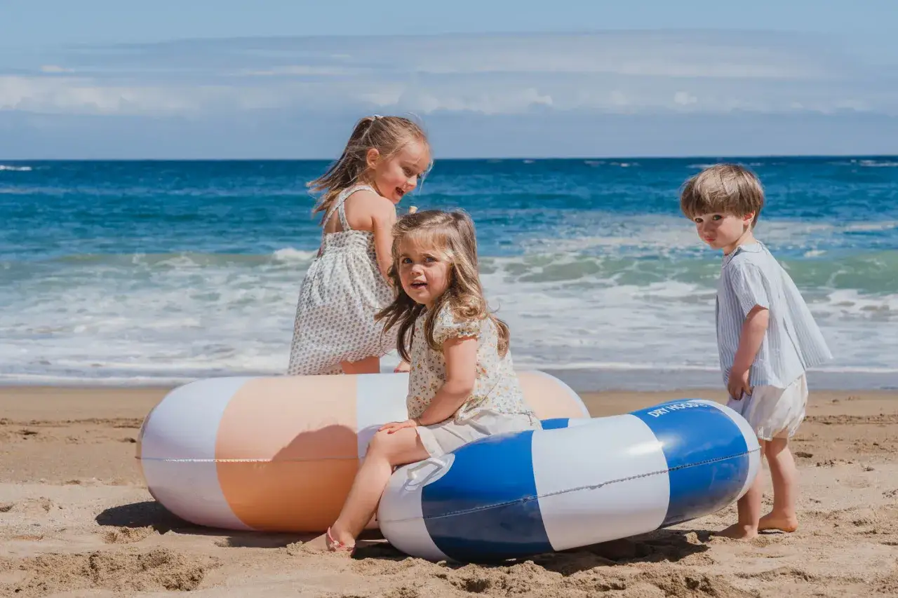 Ni&ntilde;os disfrutan de juegos en la playa con flotadores inflables, listos para la diversi&oacute;n bajo el sol y el mar azul.