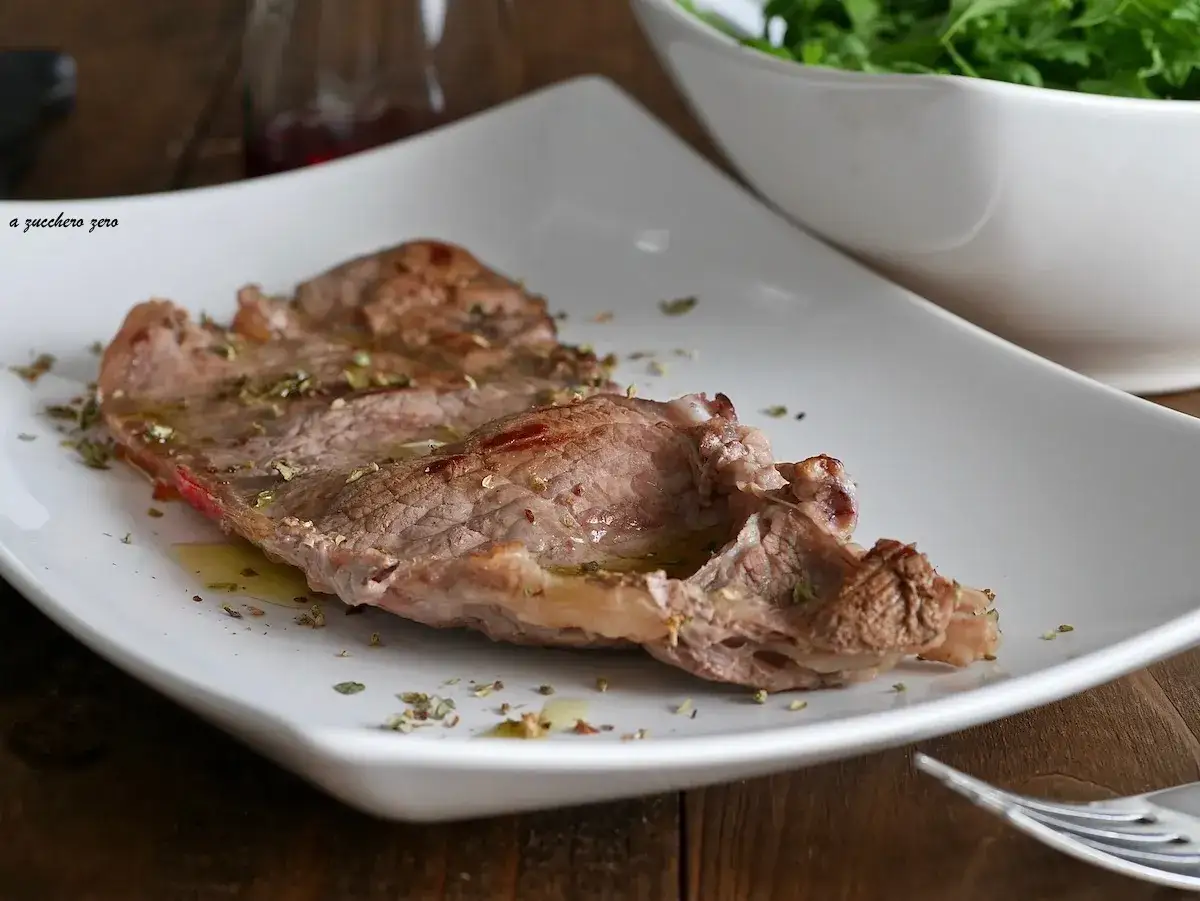 Una succulenta bistecca di manzo, condita con erbe aromatiche, servita su un piatto bianco.