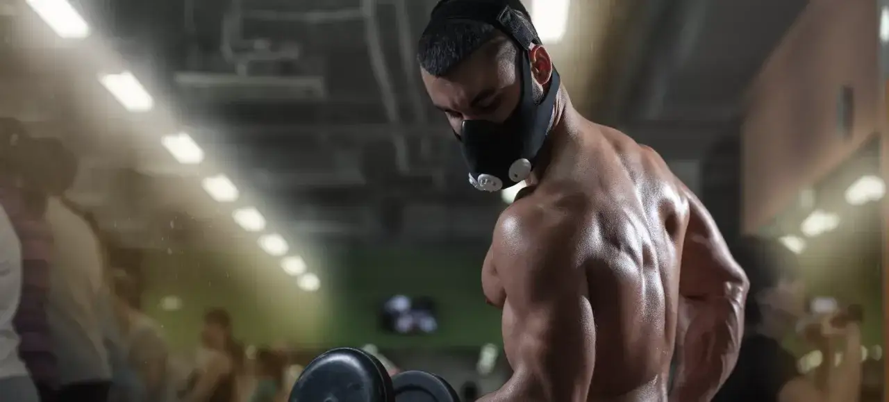 Man performing altitude mask training in a gym, lifting weights.