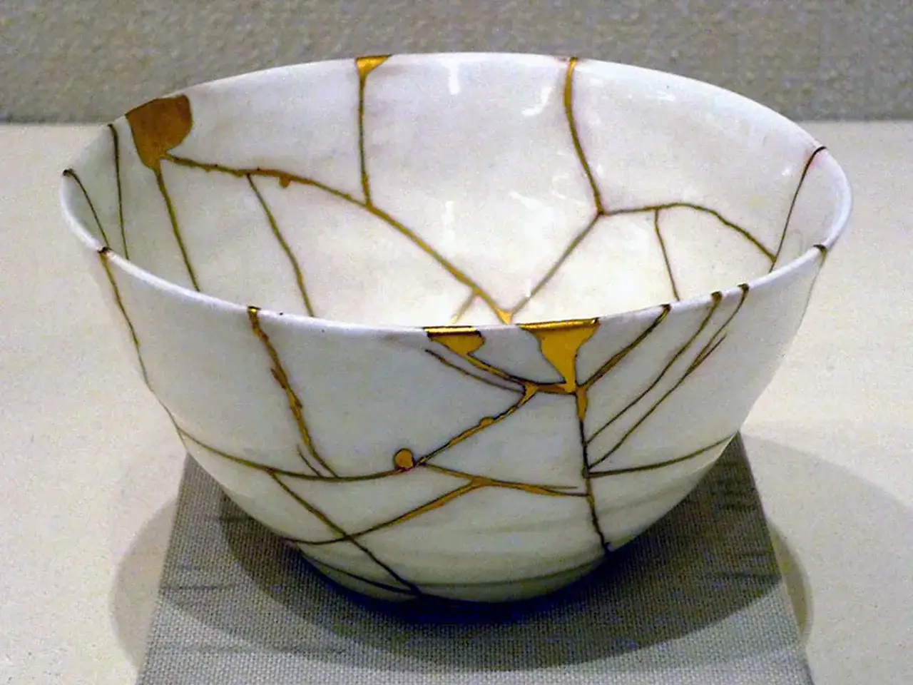 Ciotola bianca riparata con la tecnica kintsugi, le crepe dorate ne esaltano la bellezza.