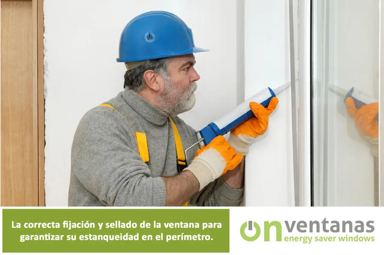 Un trabajador con casco azul aplica sellador para reparar ventanas aluminio antiguas, asegurando su estanqueidad.