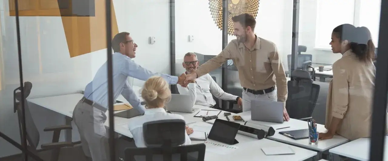 Gesch&auml;ftsleute sch&uuml;tteln H&auml;nde, feiern Erfolg und besprechen die GBR Gewinnverteilung in einem modernen B&uuml;ro.