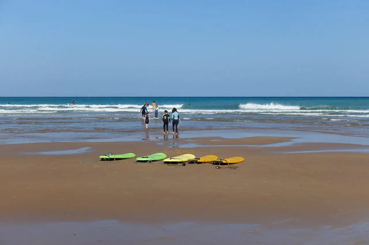 Tablas de surf en la arena y gente en el agua, un día perfecto de biarritz con niños.