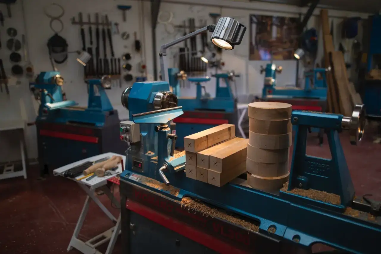 Atelier de menuiserie avec plusieurs tours à bois d'établi bleus. Des blocs de bois et des pièces cylindriques sont prêts à être travaillés.